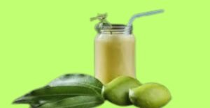 A refreshing Indian summer drinks made from raw mangoes, served in a glass jar with a straw, accompanied by fresh mangoes and green leaves on a bright background