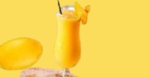 A creamy and delicious mango shake served in a tall glass with a straw, garnished with mango slices, and fresh mangoes in the background