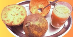 A refreshing glass of Bel Sharbat placed on a steel tray alongside fresh bell fruits, both whole and cut open, showcasing their pulp