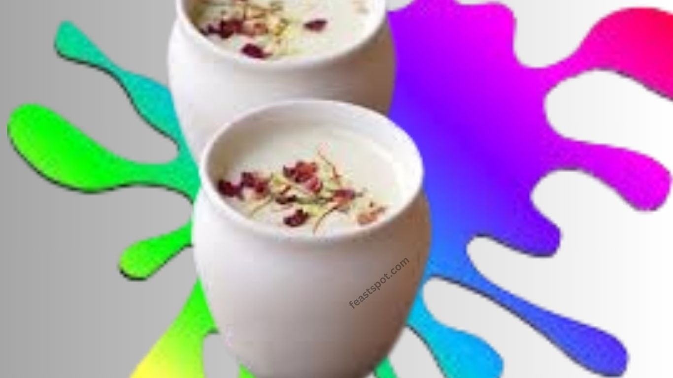 Two cup of colorful Holi special thandai topped with rose petals, pistachios, and almonds, with vibrant Holi colors splashed around