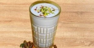 A tall glass of creamy and refreshing lassi, garnished with chopped pistachios and saffron, a popular Indian yogurt-based summer drin